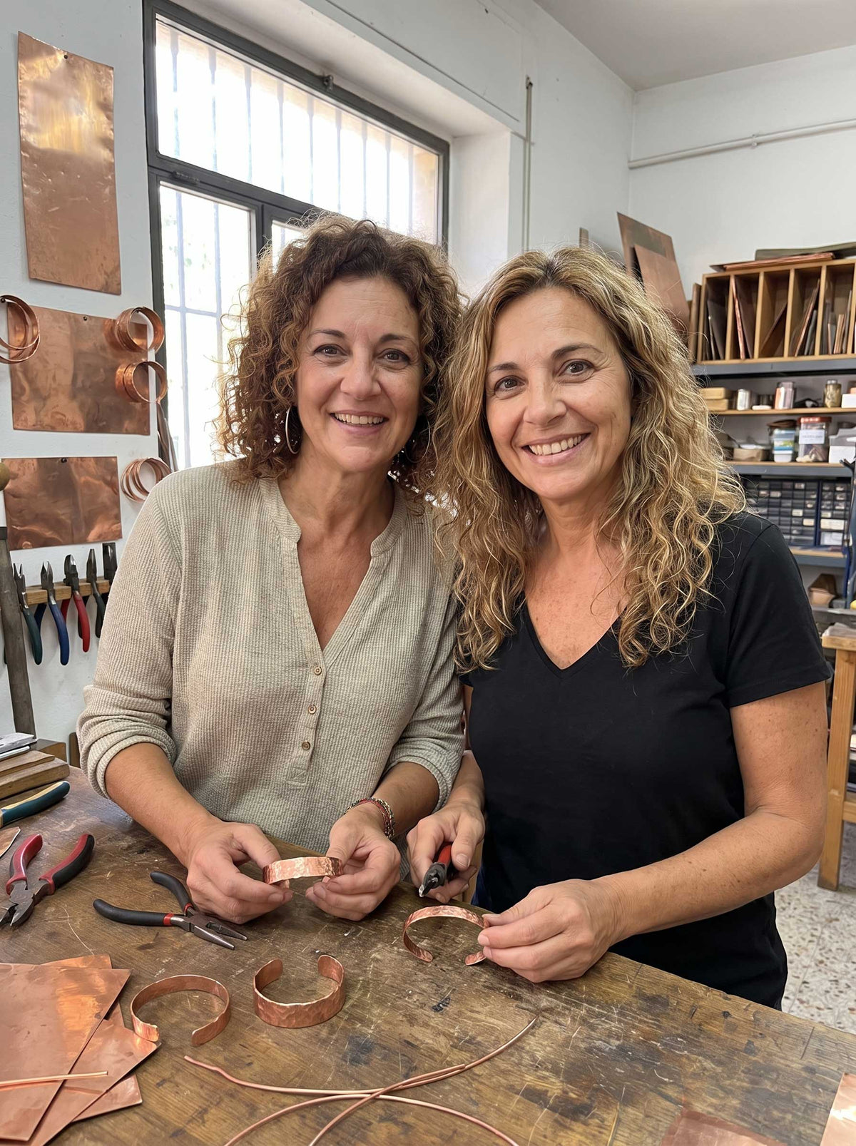 Dos mujeres trabajan brazaletes de cobre en un banco de madera